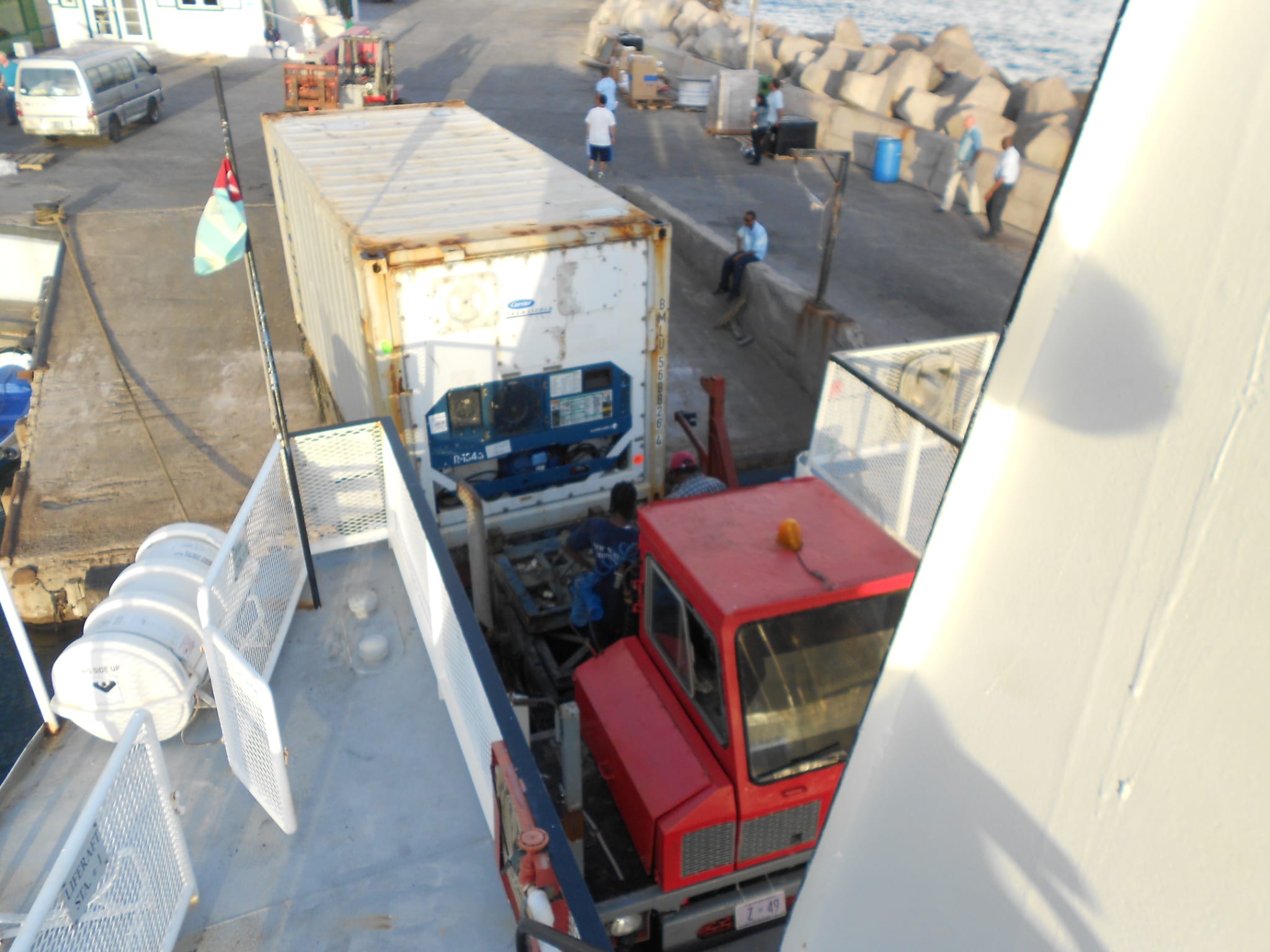 Container refrigerato scaricato da una nave su un mezzo pesante in banchina, con operatori al lavoro