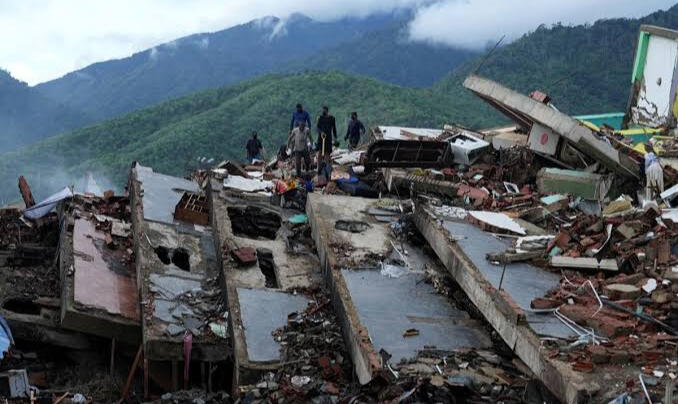Persone al lavoro sulle macerie di edifici crollati dopo il terremoto, con le montagne sullo sfondo